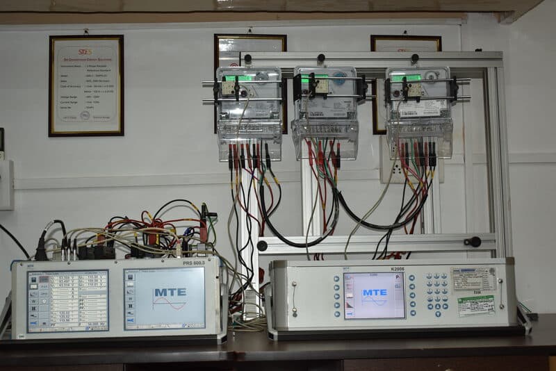 SDES technician operating MTE energy meter calibration setup with three meters mounted on test frame