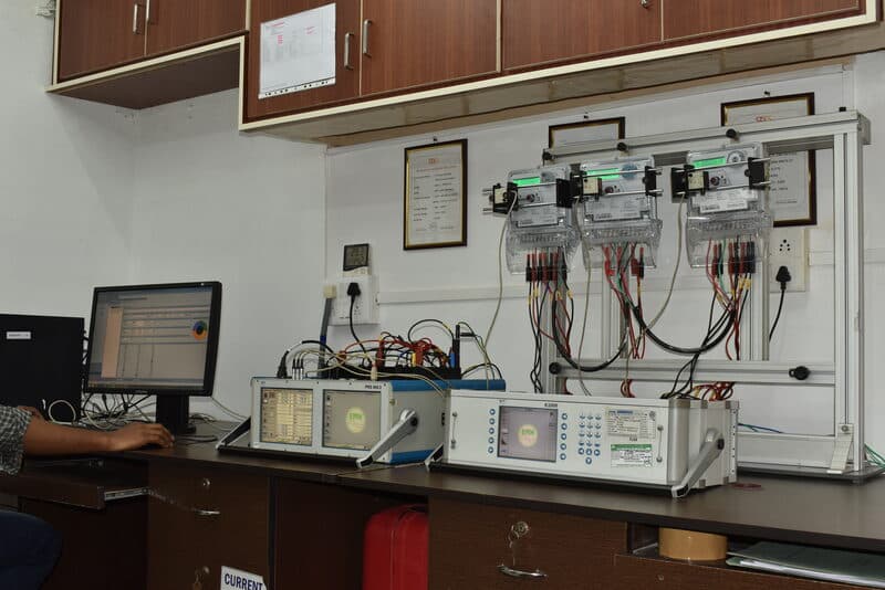 Energy meter calibration bench with EMH reference standards and NABL certificates on the wall at SDES lab
